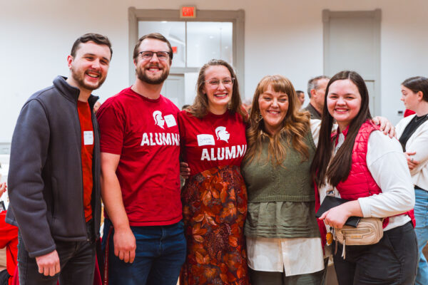 A group of alumni students stand with a professor.