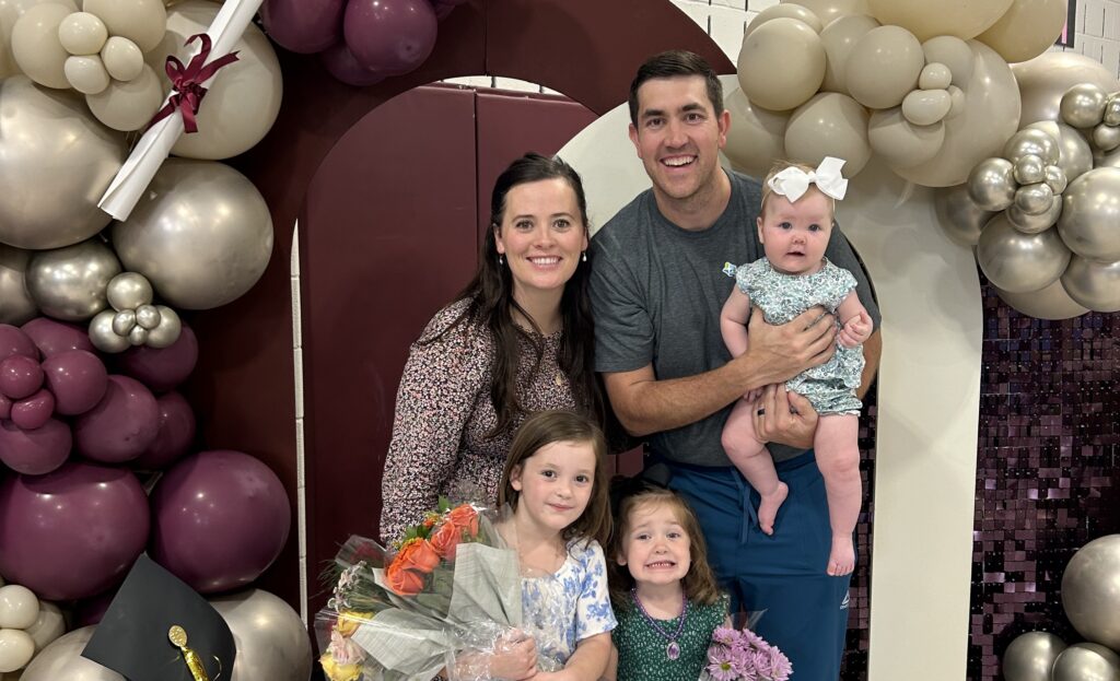 A family stands under an arch of balloons