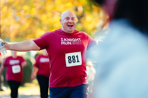 A smiling man runs with his arms outstretched.